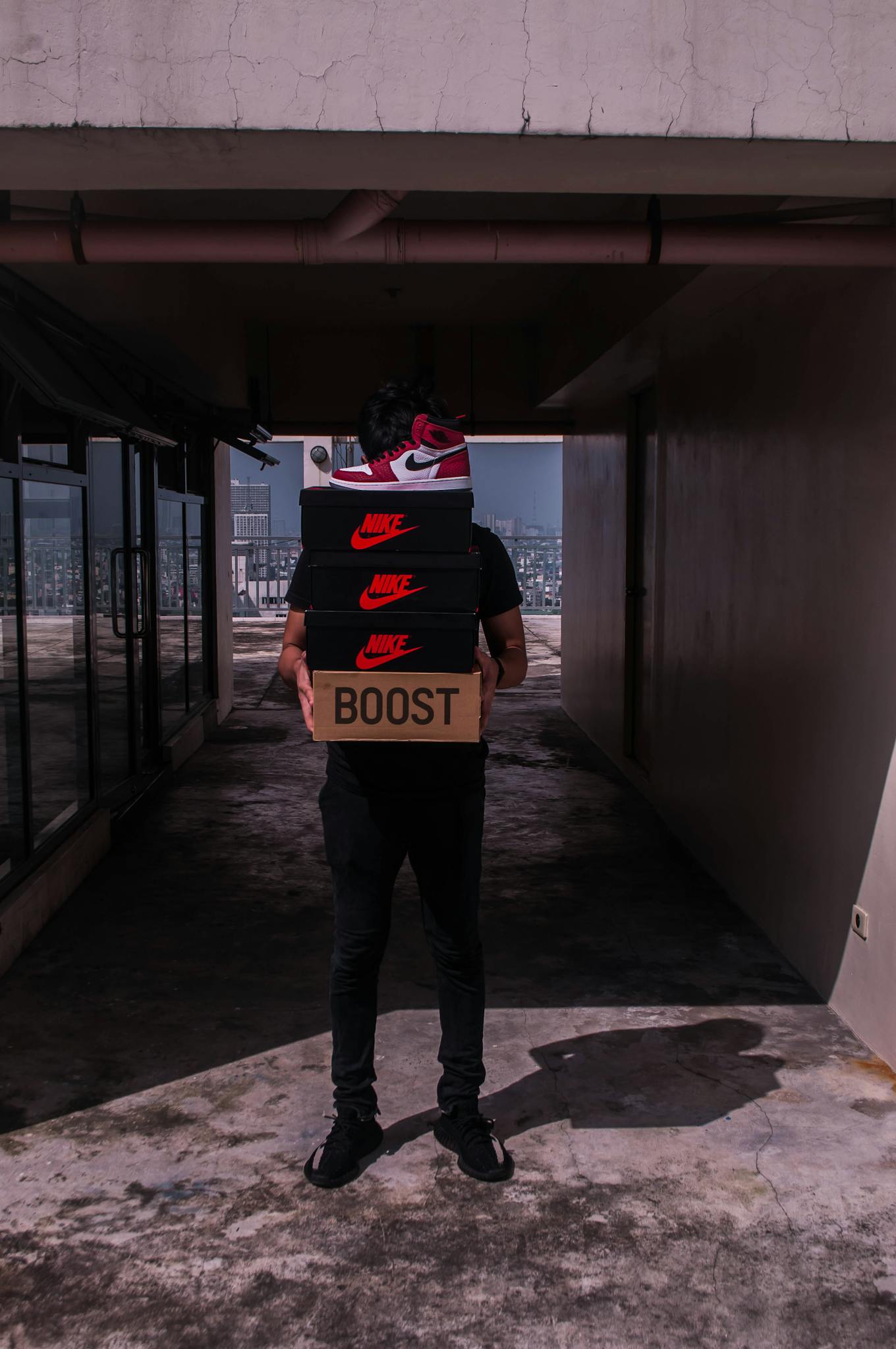 Man carrying shoe boxes with branded labels in an outdoor hallway setting.