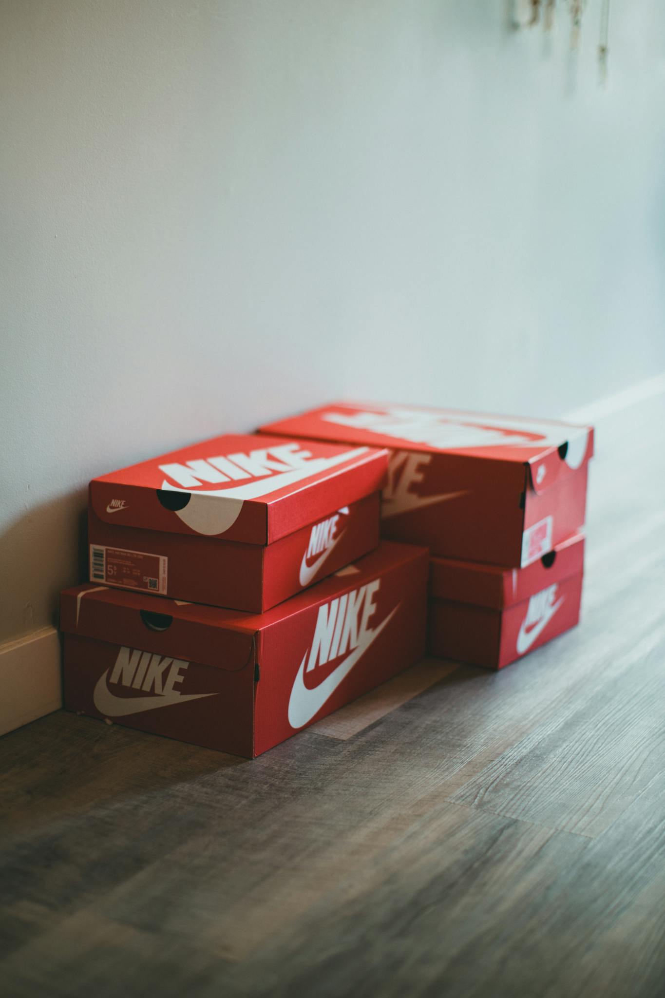 Red Nike shoe boxes stacked on a wooden floor indoors.