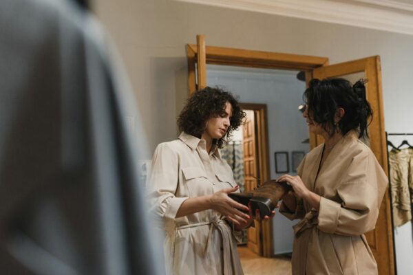 Two women engaged in shopping discussion over a leather boot in a stylish fashion boutique.